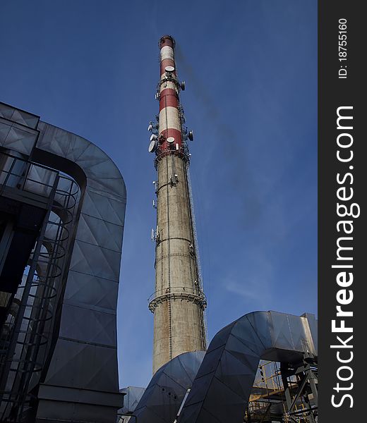 A tall chimney with smoke visible against the blue sky