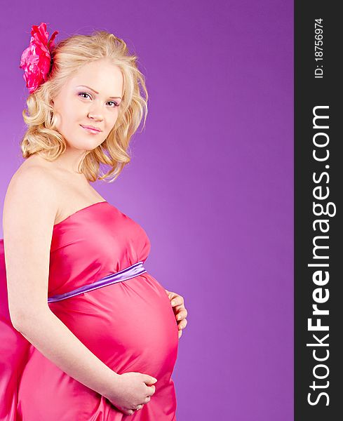 A young pregnant woman in a pink dress on the purple background. A young pregnant woman in a pink dress on the purple background