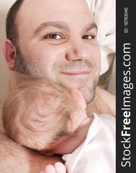 A father cuddles his newborn baby on his shoulder and looks at camera. A father cuddles his newborn baby on his shoulder and looks at camera