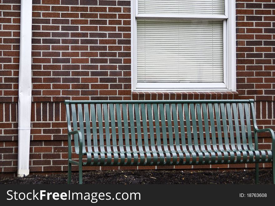 A green park bench next to a red brick wall.