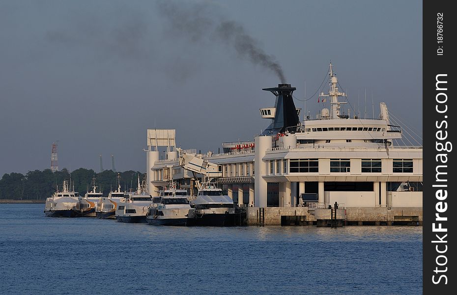 Ferry terminal with a big ship releasing black smoke from it's funnel.