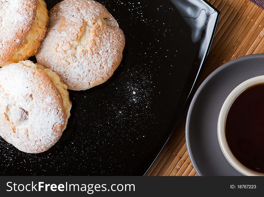 Muffins with a sugar powder on a black plate and a cup of tea