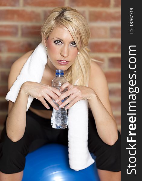 A young pretty girl sitting on an exercise ball drinking water after workout. A young pretty girl sitting on an exercise ball drinking water after workout