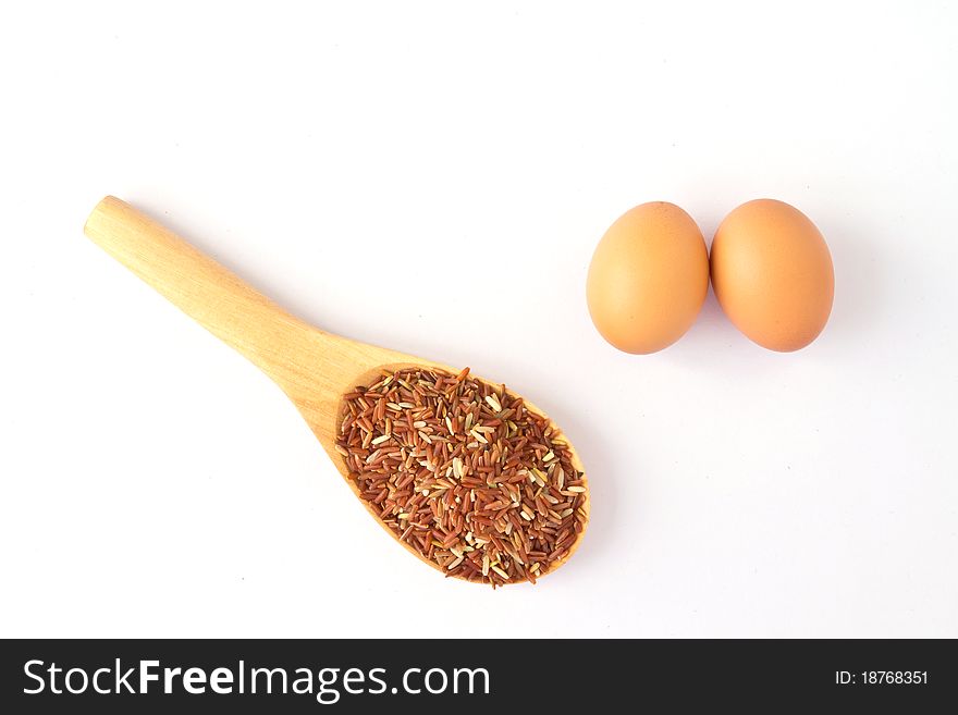 Brown egg and wooden spoon with red rice; on a white background