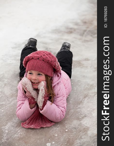 The smiling girl in pink cap and scarf slides on icy descent. The smiling girl in pink cap and scarf slides on icy descent