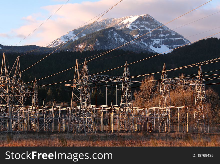 Electric power lines and power station from the Bonneville Dam on the Columbia River. Pink clouds in blue sky, snowy hillside. Electric power lines and power station from the Bonneville Dam on the Columbia River. Pink clouds in blue sky, snowy hillside.