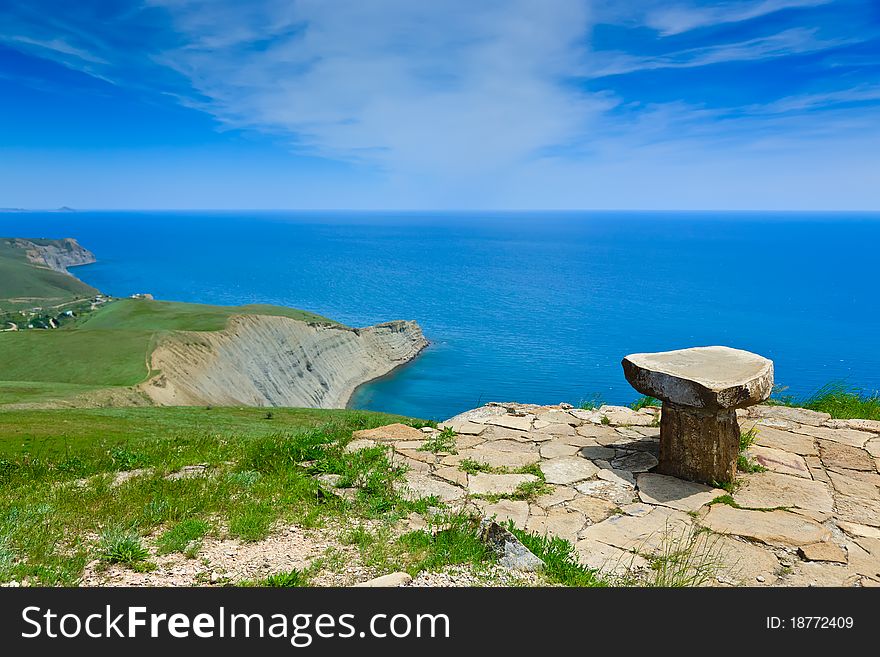 Stone seat on mountain above the sea on a background of the sky with clouds. Stone seat on mountain above the sea on a background of the sky with clouds