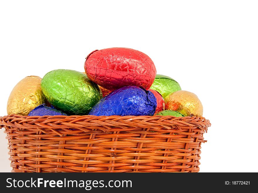 Colorful easter eggs wrapped in shiny foil in wicker basket isolated white background. Colorful easter eggs wrapped in shiny foil in wicker basket isolated white background