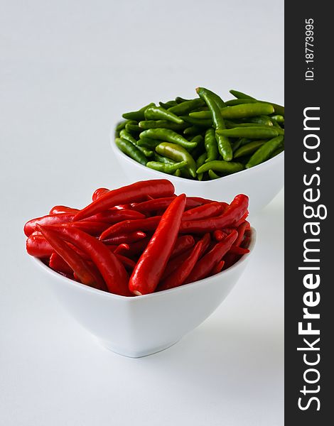 Red and green chili peppers in white cups on white background