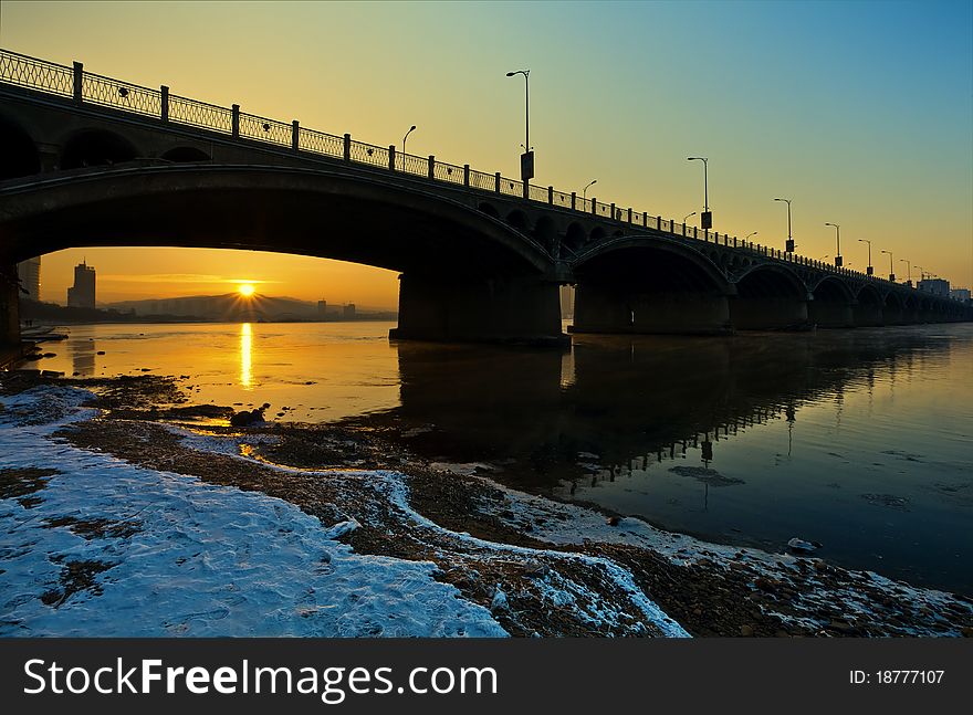 Winter sunset over big wide river with bridge.
