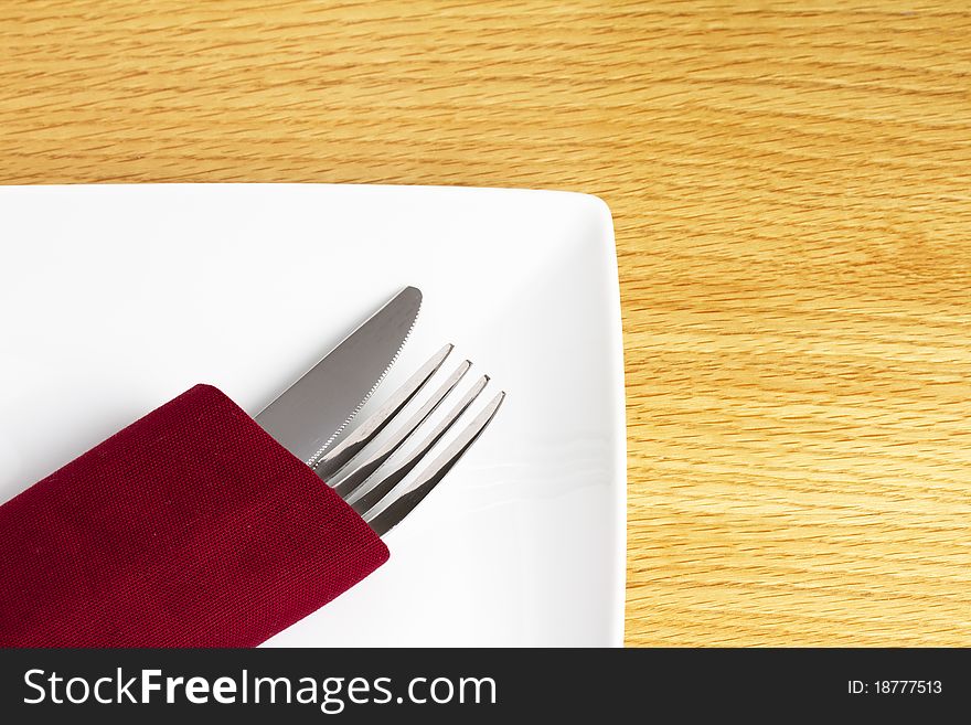 Knife and fork in red napkin on plate