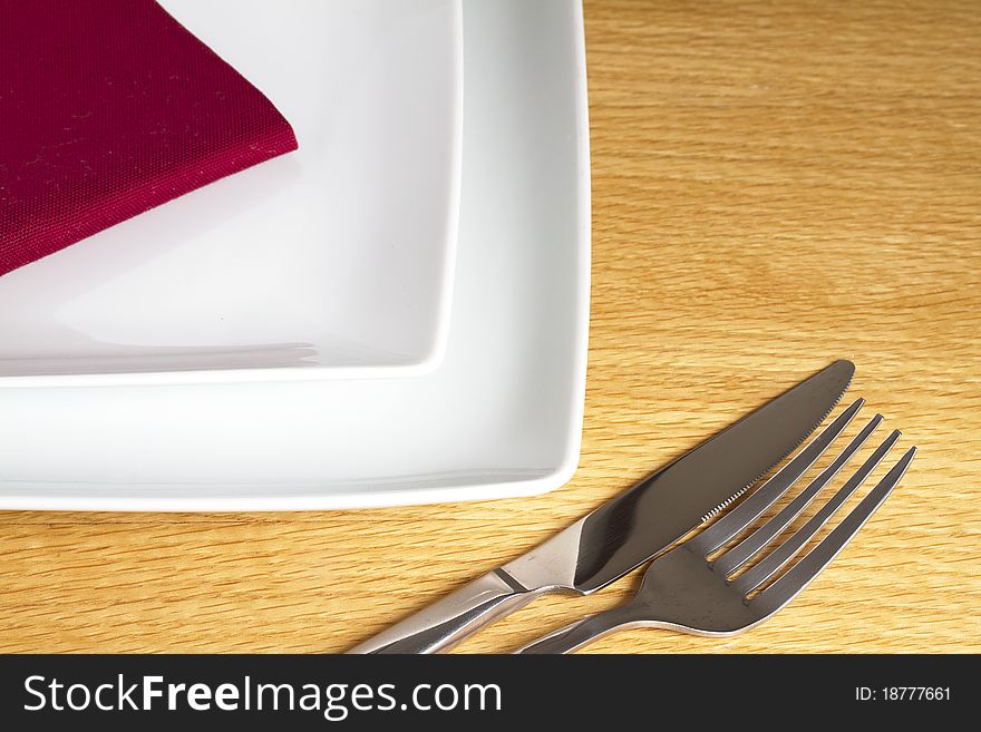 Kinfe and fork on table with red napkin and white plates. Kinfe and fork on table with red napkin and white plates