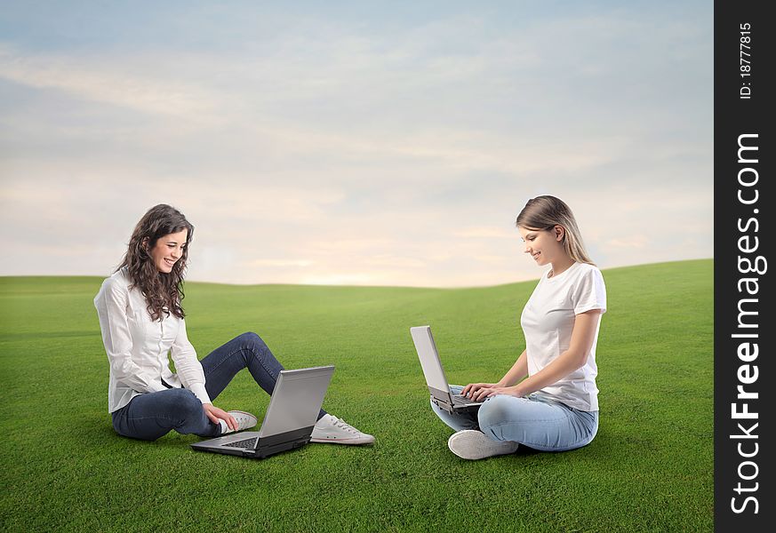 Beautiful women using laptops on a green meadow. Beautiful women using laptops on a green meadow
