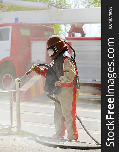 Worker in a protective suit spraying sand with abrasive peeler