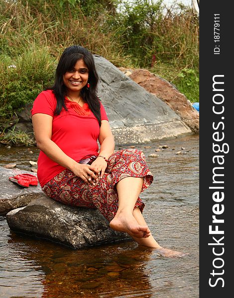 Young indian woman in casual red dress sitting on a rock in water. Young indian woman in casual red dress sitting on a rock in water