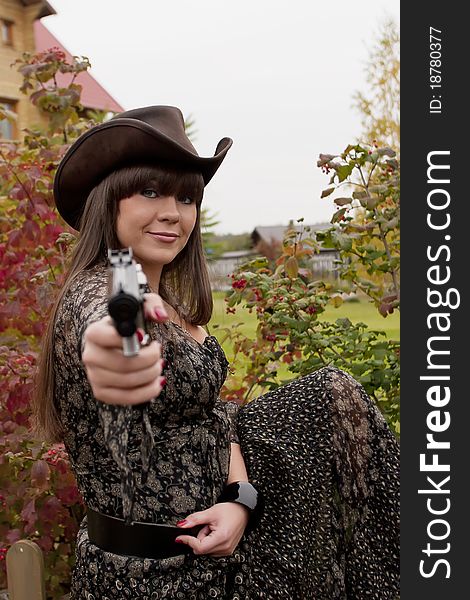 Young girl wearing long dress and leather hat points her gun toward the viewer. Young girl wearing long dress and leather hat points her gun toward the viewer