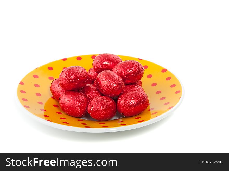 Chocolate easter eggs in red foil on a dotted saucer isolated over white