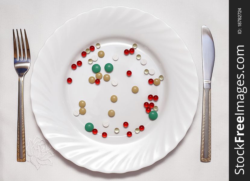 Vitamin photo on a white plate, the fork and a knife nearby lie. Vitamin photo on a white plate, the fork and a knife nearby lie