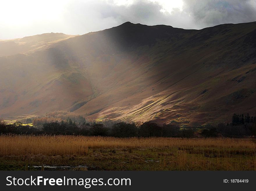 Sun breaks through the winter cloud and illuminates a dark fell. Lake District, Cumbria, England. Sun breaks through the winter cloud and illuminates a dark fell. Lake District, Cumbria, England.