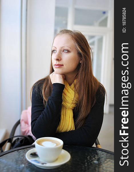 Young woman sits at table in cafe. Drinks coffee
