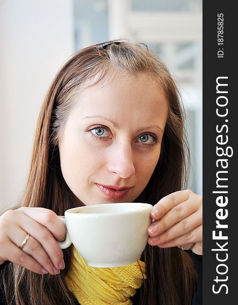 Young woman holding cup of coffee and looking out window. She drinks coffee at cafe