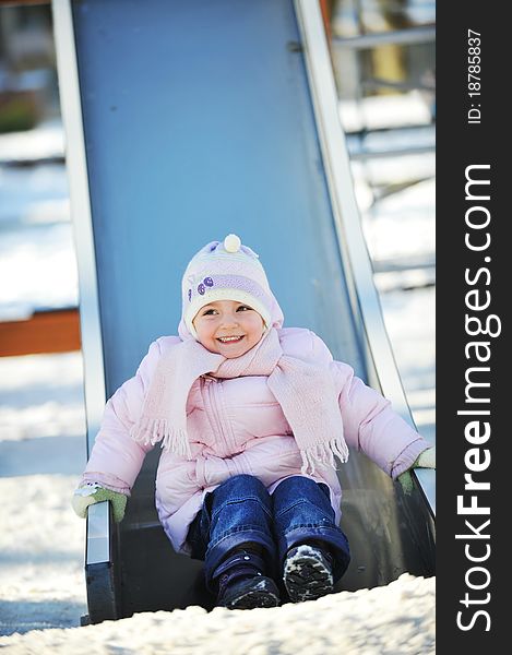 Small beautiful girl sits on  children's hill. Winter day