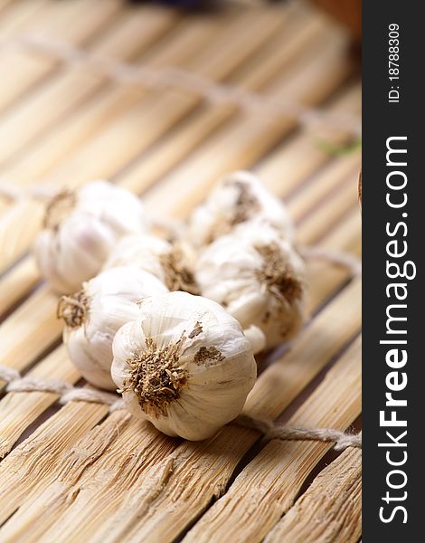 Closeup shot of white garlic pods over wooden mat.
