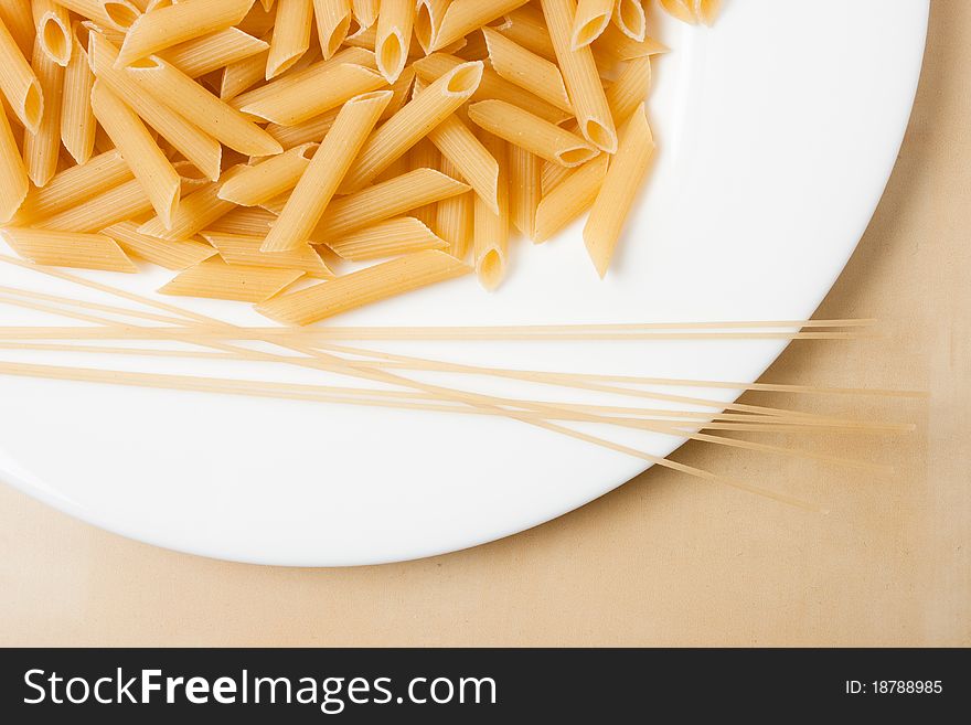 Raw pasta on white plate, on wooden table