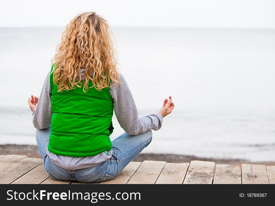 Yoga woman sitting on wooden bridge near the ocean