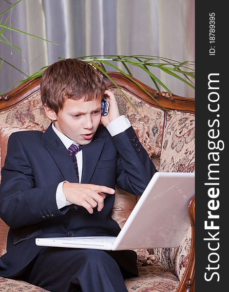 Young angry confident businessman talking on cell pointing at computer. Young angry confident businessman talking on cell pointing at computer