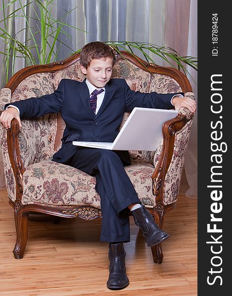 Young smiling boy dressed in business suite looking at white notebook. Young smiling boy dressed in business suite looking at white notebook