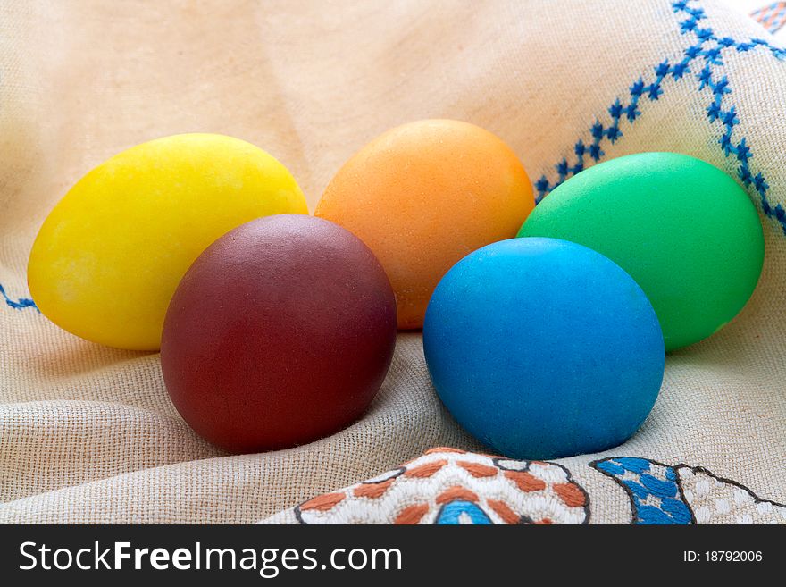 Five Easter  painted eggs (blue, yellow,  orange,  violet, green) on unbleached linen with embroidery. Five Easter  painted eggs (blue, yellow,  orange,  violet, green) on unbleached linen with embroidery