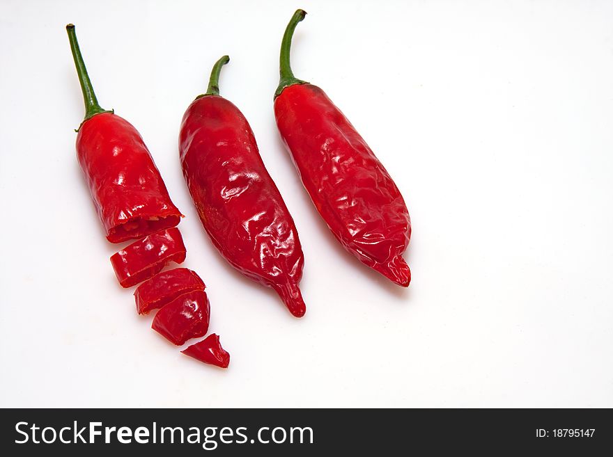 Three red chili peppers on white background, one is cut