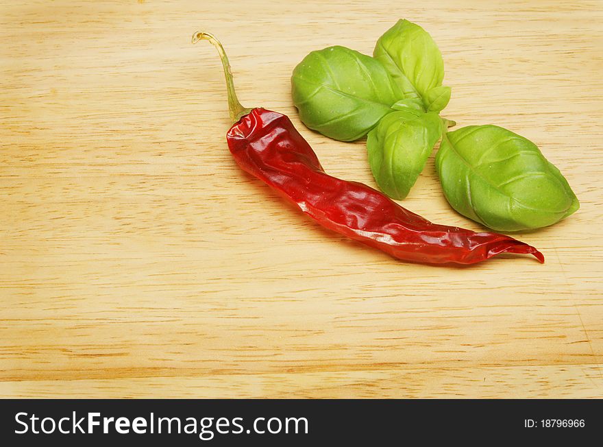 Dried chilli pepper and fresh basil leaves on a wooden food preparation board. Dried chilli pepper and fresh basil leaves on a wooden food preparation board