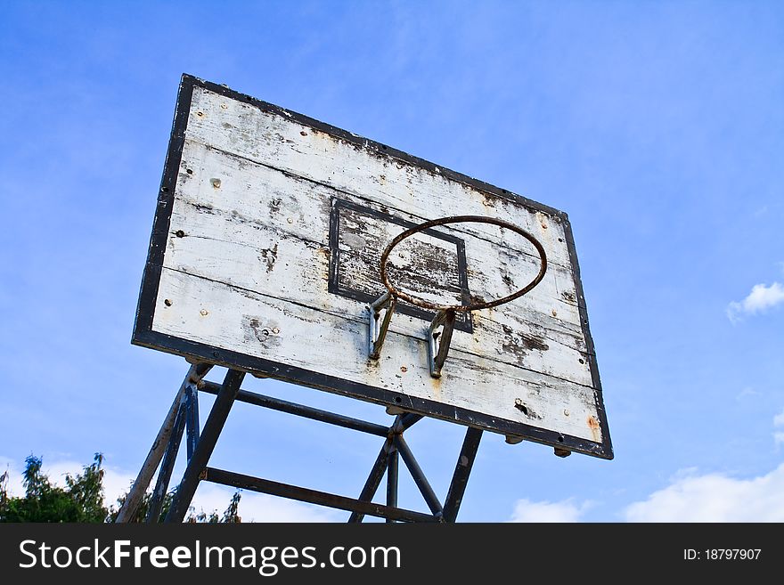 Old outdoor basketball hoop against blue sky background