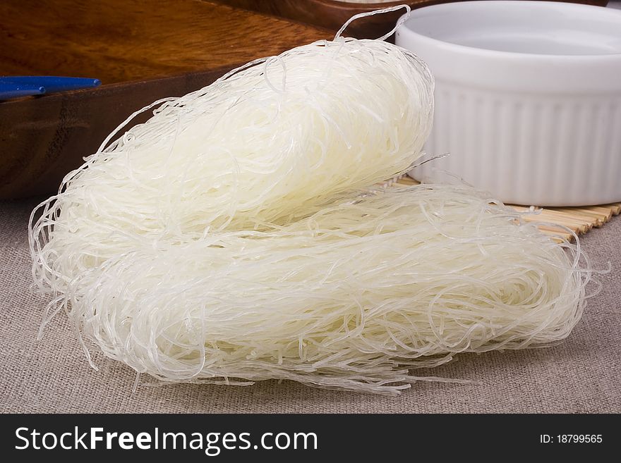 Close-up of raw white rice noodles on brown background.