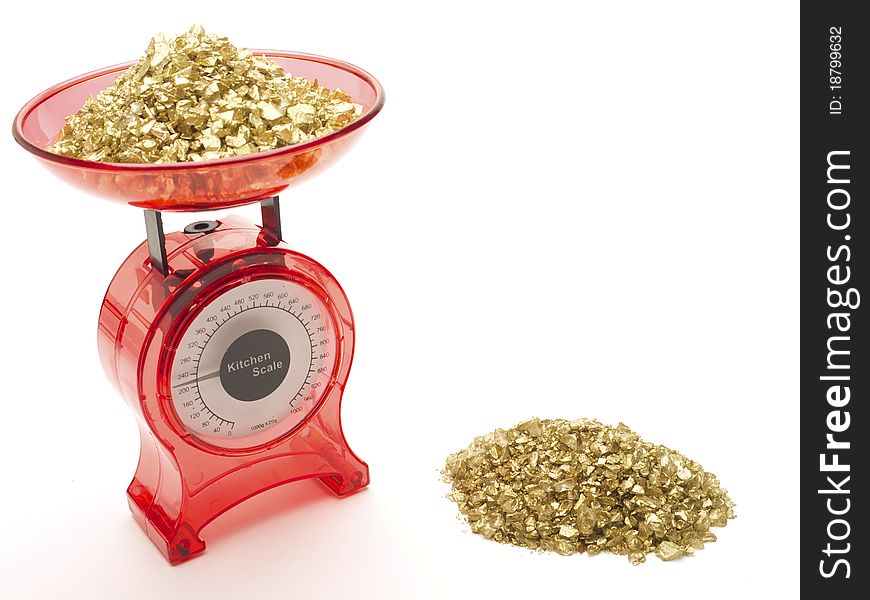 Red kitchen scales with a pile of gold being weighed and a pile of gold by the side of it