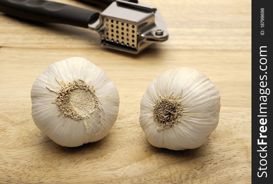 Garlic press and two cloves of garlic, shot on a wooden background