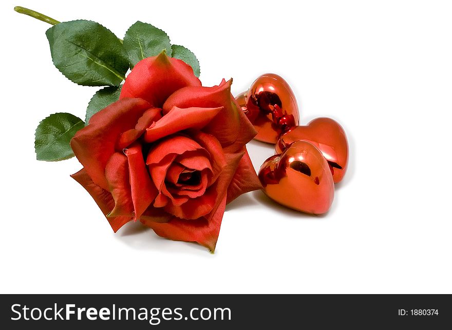 Red rose isolated on white with three little shinny red heart shaped ornaments lying along side it. Red rose isolated on white with three little shinny red heart shaped ornaments lying along side it.