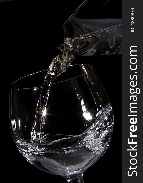 Water pouring from a decanter into a glass on black backrougnd. Water pouring from a decanter into a glass on black backrougnd