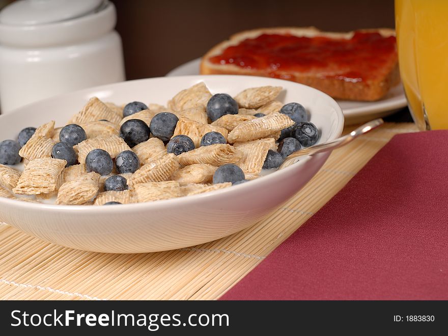 A bowl of wheat cereal with blueberries, toast and orange juice