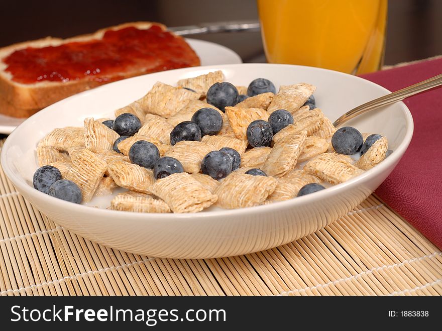 A bowl of wheat cereal with blueberries, toast and orange juice