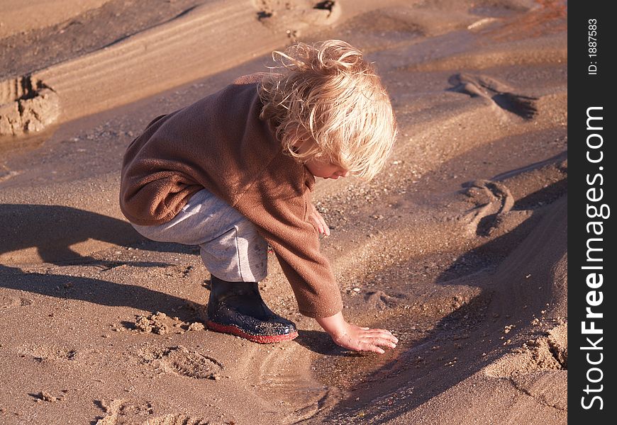 A small boy plays at the beach in a sandy beach puddle. Totally immersed in what he is doing. A small boy plays at the beach in a sandy beach puddle. Totally immersed in what he is doing.