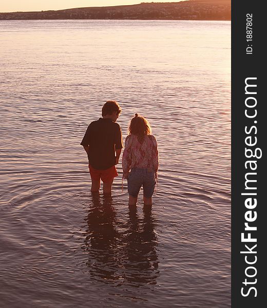 Two children look down into the sea where they are standing, exploring. Two children look down into the sea where they are standing, exploring.