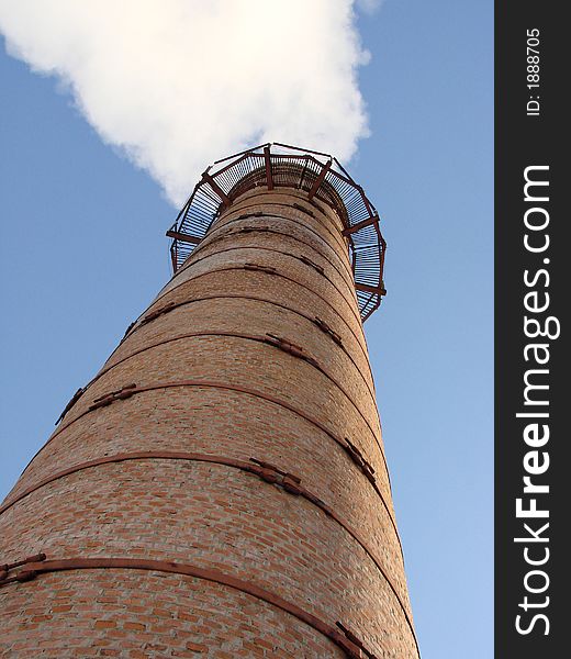 Old steaming industrial tube against blue sky