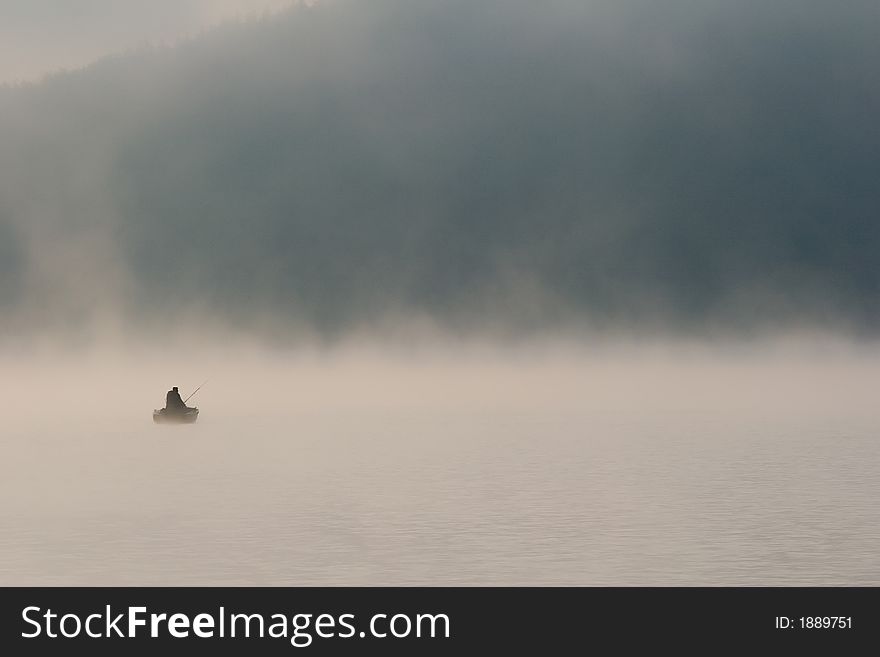 Lonely fisherman on misty lake