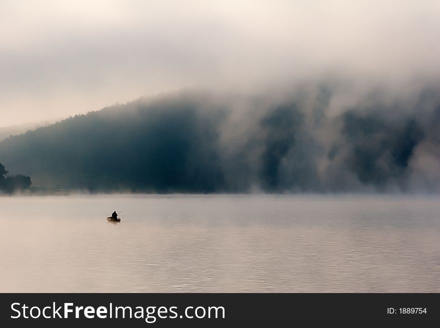 Lonely fisherman on misty lake