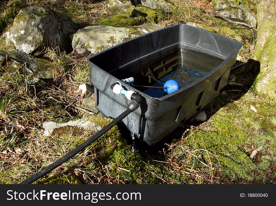 A black water tank, half full, with a pipe and ball in an outdoor situation. A black water tank, half full, with a pipe and ball in an outdoor situation.