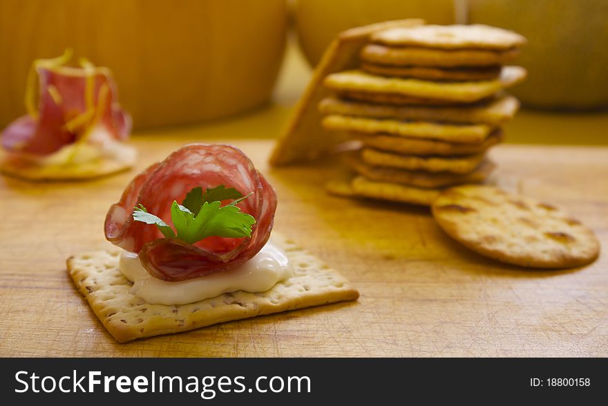 Pile of crackers with one served with Italian meat, shot on a wooden table