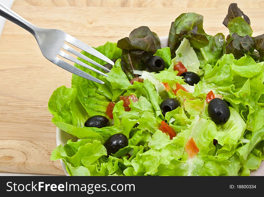 Greek salad style in plate with fork on wood background